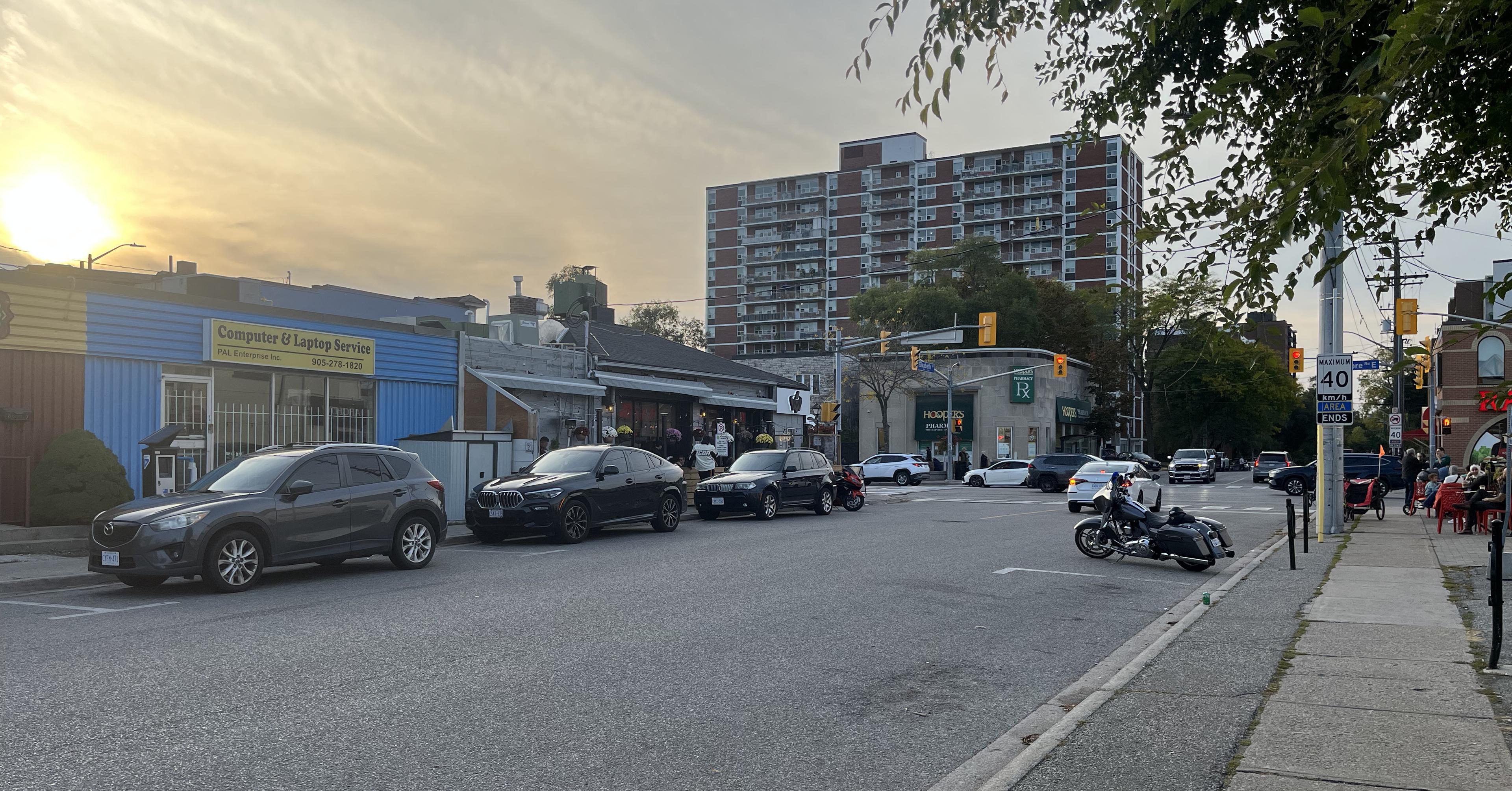 Sunset view of Lakeshore Road East and Elizabeth Street in Port Credit, Mississauga, showing local shops, parked cars, and a motorcycle near the intersection.